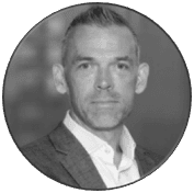 Circular black and white headshot of a man wearing a suit and collared shirt.