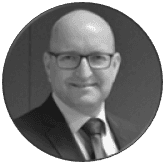 Circular grayscale portrait of a bald man wearing glasses, a suit, and a tie.